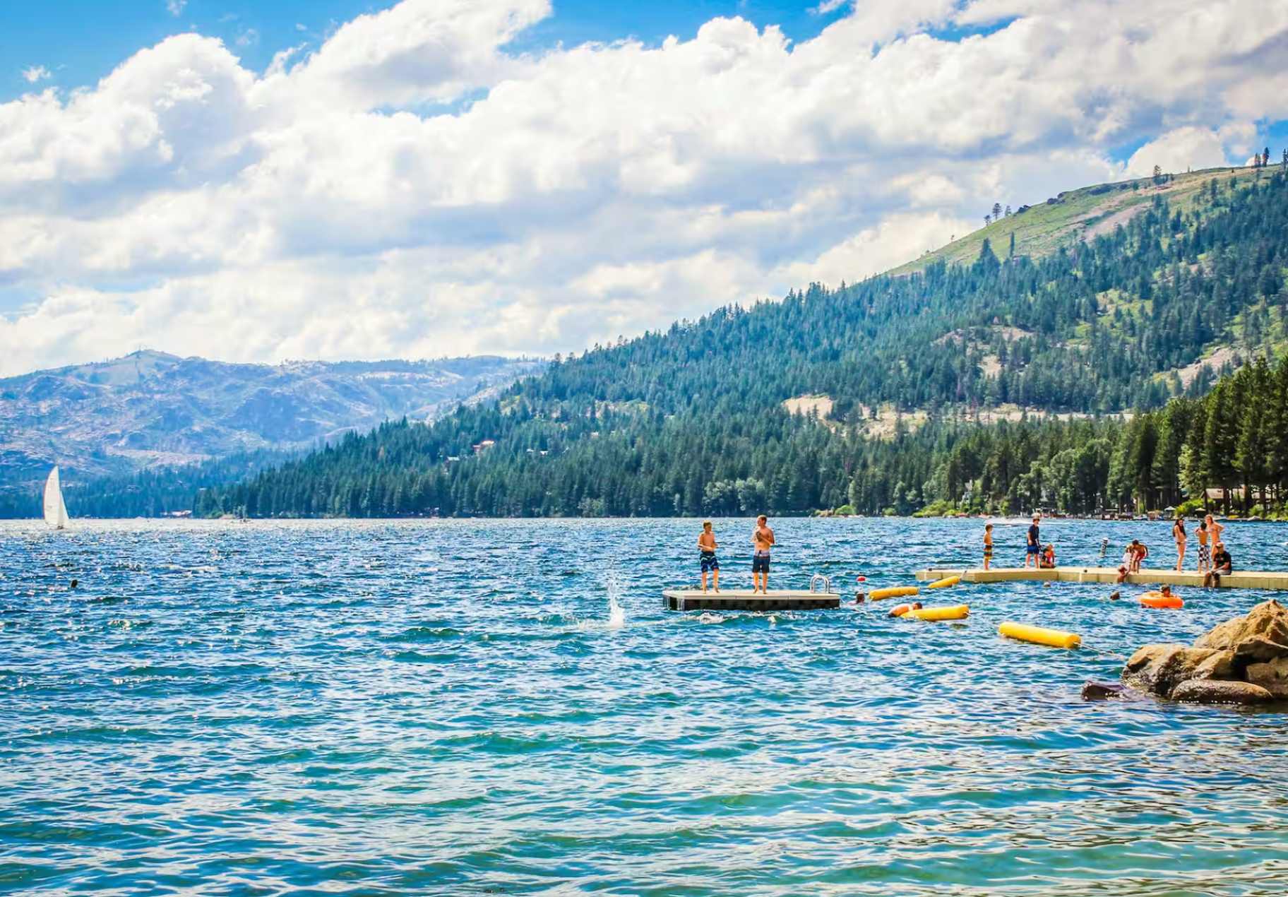 Lakefront scene in Truckee with mountains, swimmers, and a pier; ideal for a vacation rental.