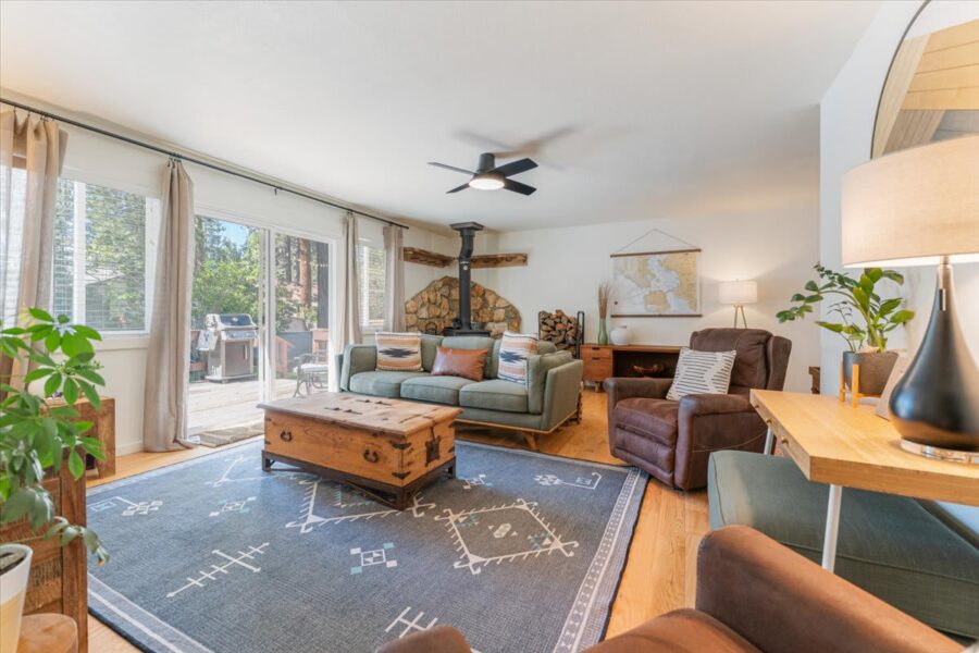Cozy living room in a Truckee vacation rental, featuring rustic decor, large windows, and a wood-burning stove.