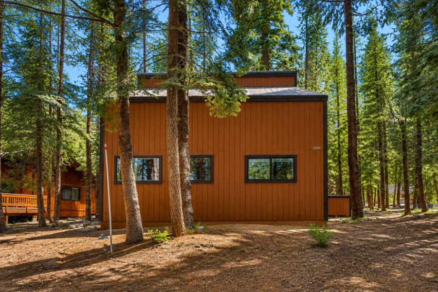 Wooden vacation rental nestled among pine trees in Truckee, with three rectangular windows and a forest backdrop.