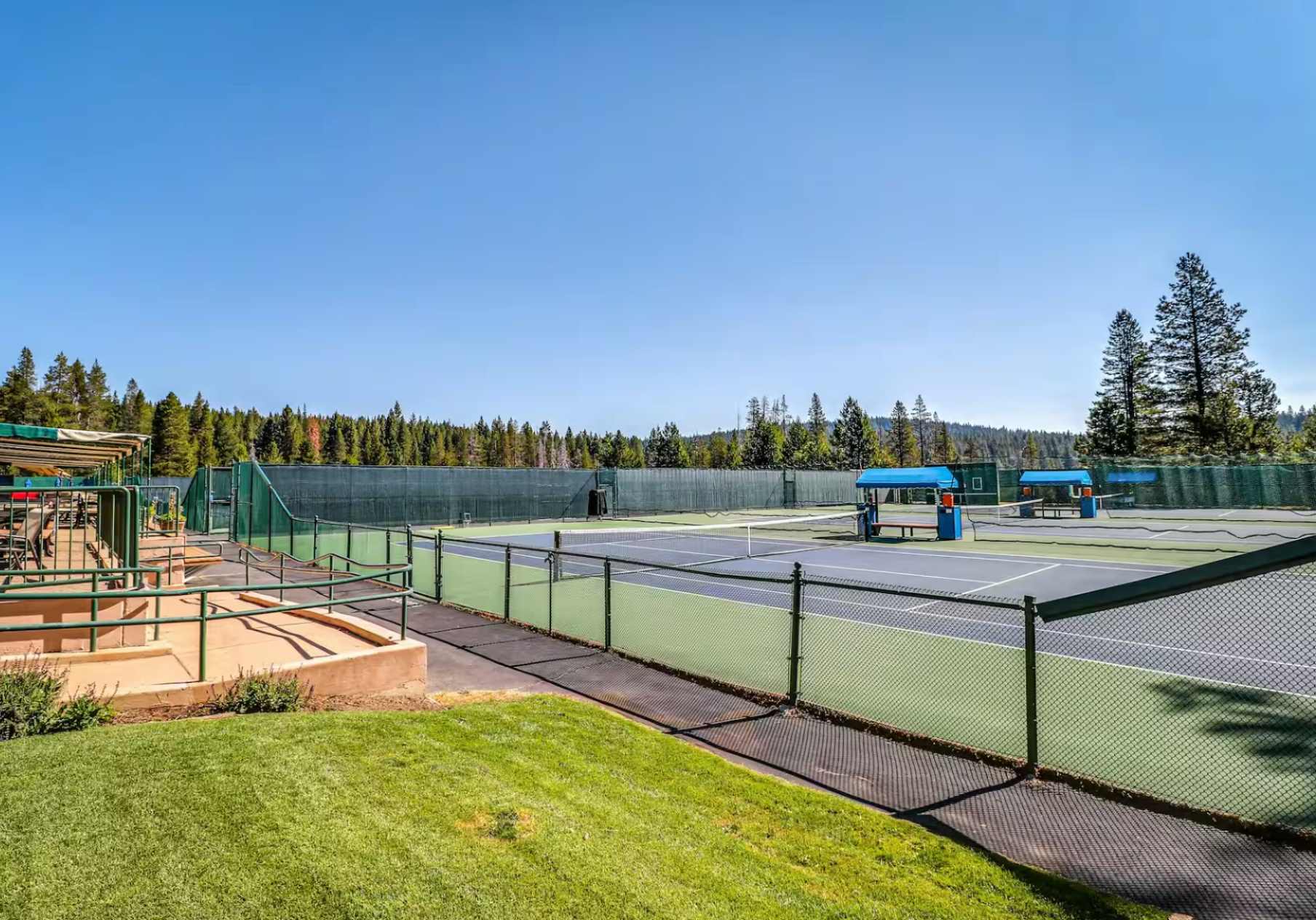 Tennis courts surrounded by pine trees at Truckee vacation rental, under a clear blue sky.