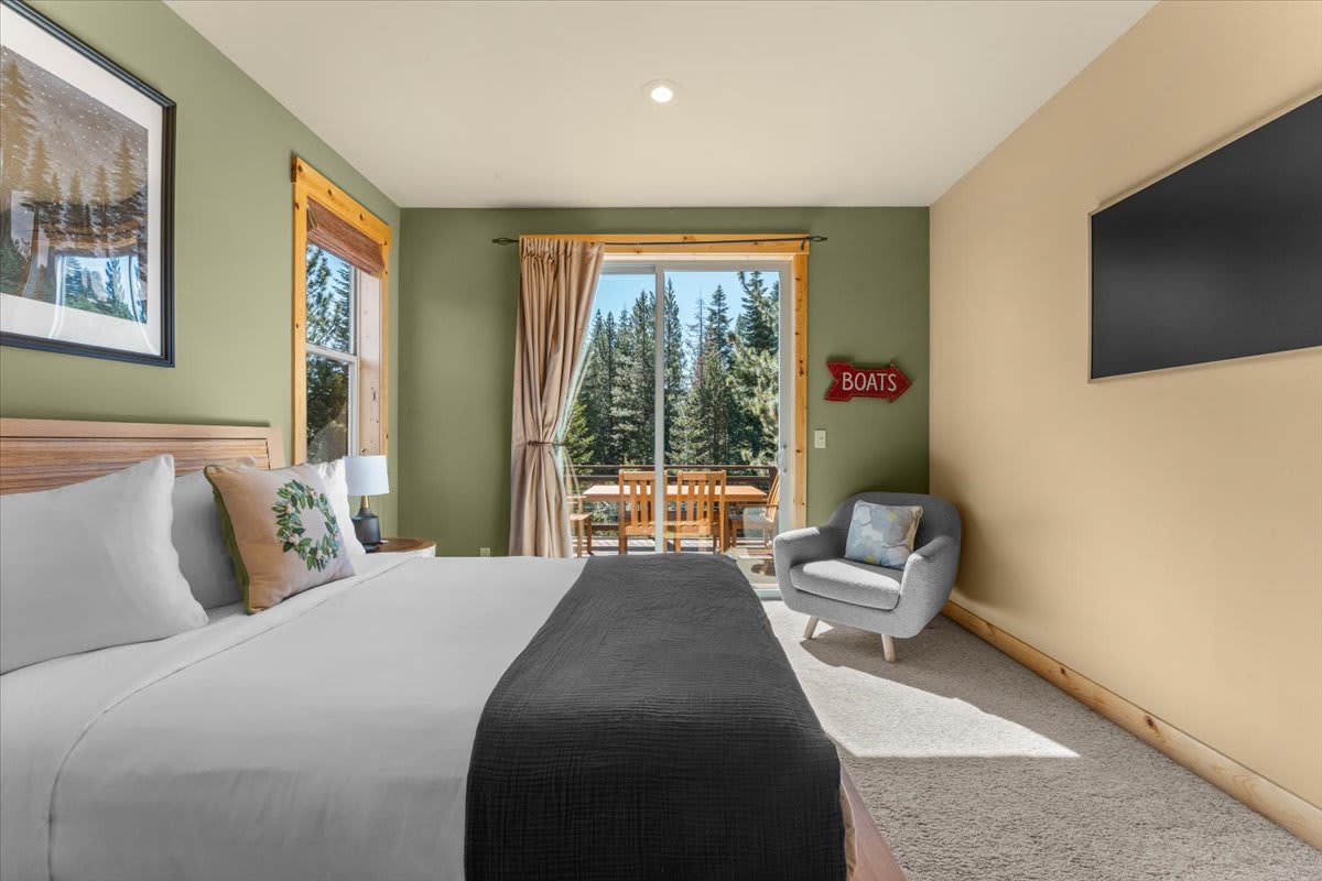 Cozy bedroom in Truckee vacation rental with forest view, featuring a comfy bed, armchair, and balcony access.