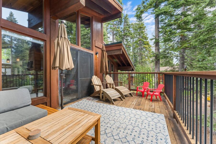 Spacious deck at a vacation rental in Carnelian Bay, featuring wooden furniture and surrounded by tall trees.