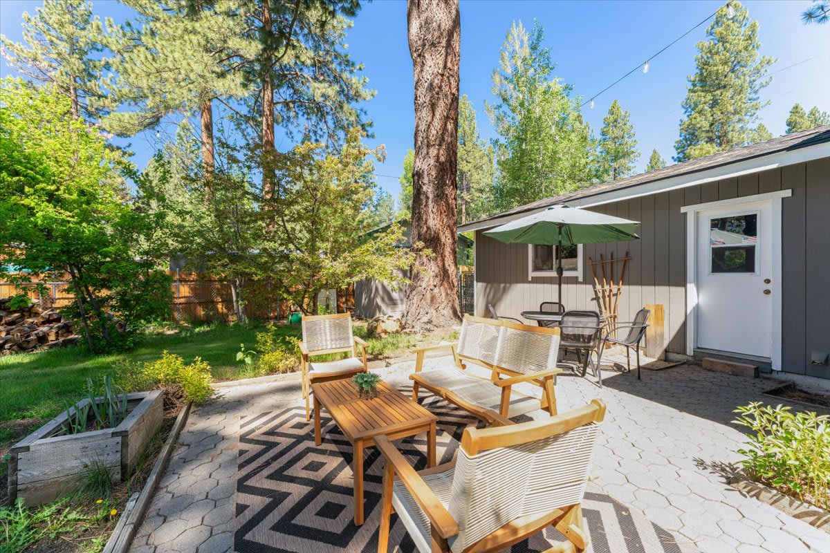 Cozy patio of a Truckee vacation rental with outdoor seating, umbrella, and lush trees in the backyard.