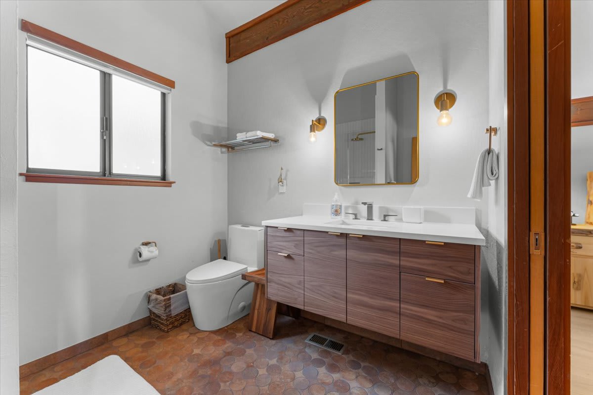 Modern bathroom in a Carnelian Bay vacation rental with wooden cabinets, large mirror, and stylish lighting.