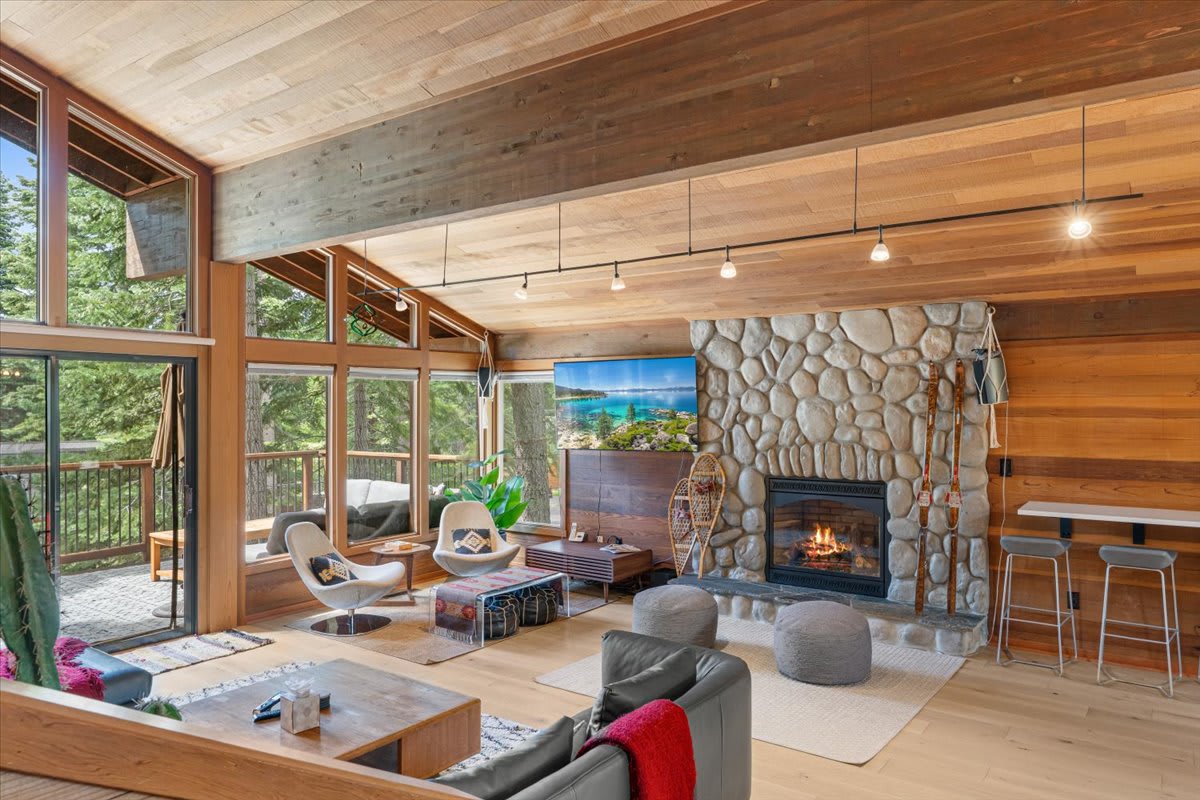 Cozy living room in a Carnelian Bay vacation rental with a stone fireplace and large windows overlooking a forested view.