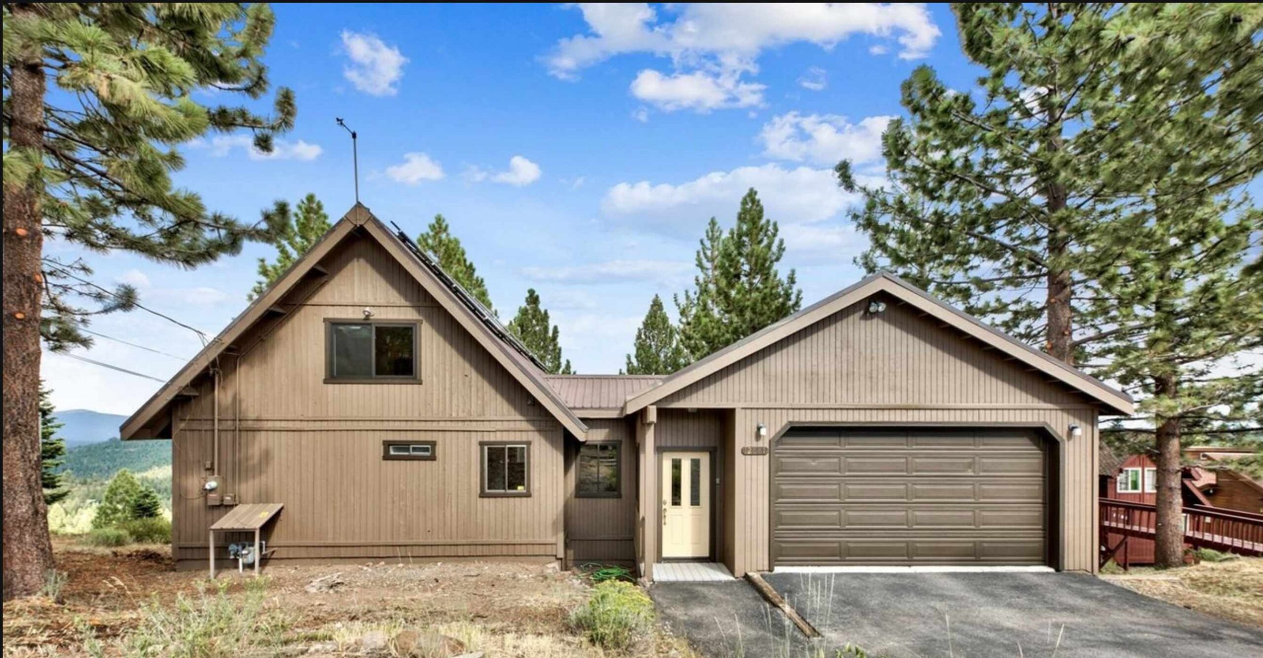 A charming cabin-style vacation rental in Truckee, surrounded by tall pine trees under a bright blue sky.