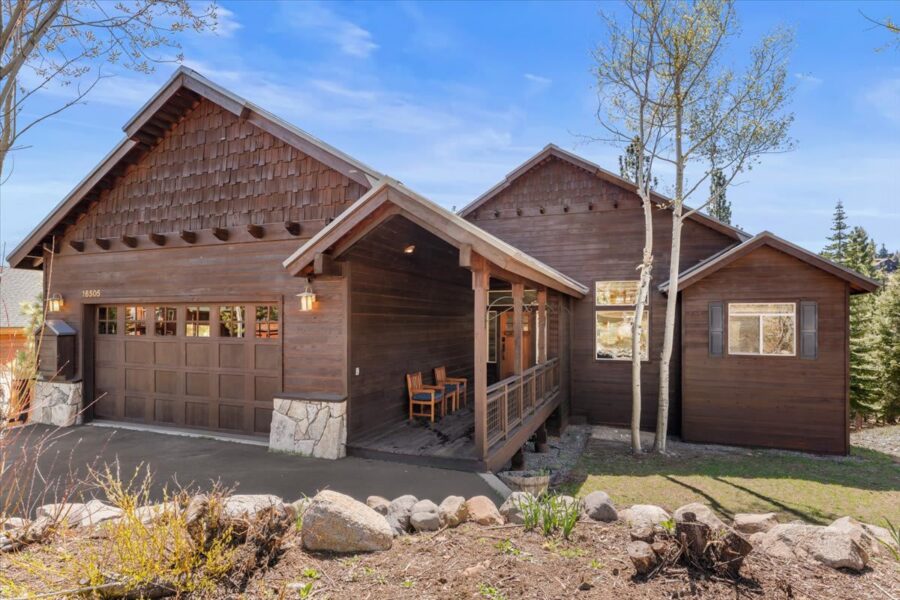 Cozy cabin-style vacation rental in Truckee, featuring a wooden exterior, porch, and garage amidst a scenic landscape.