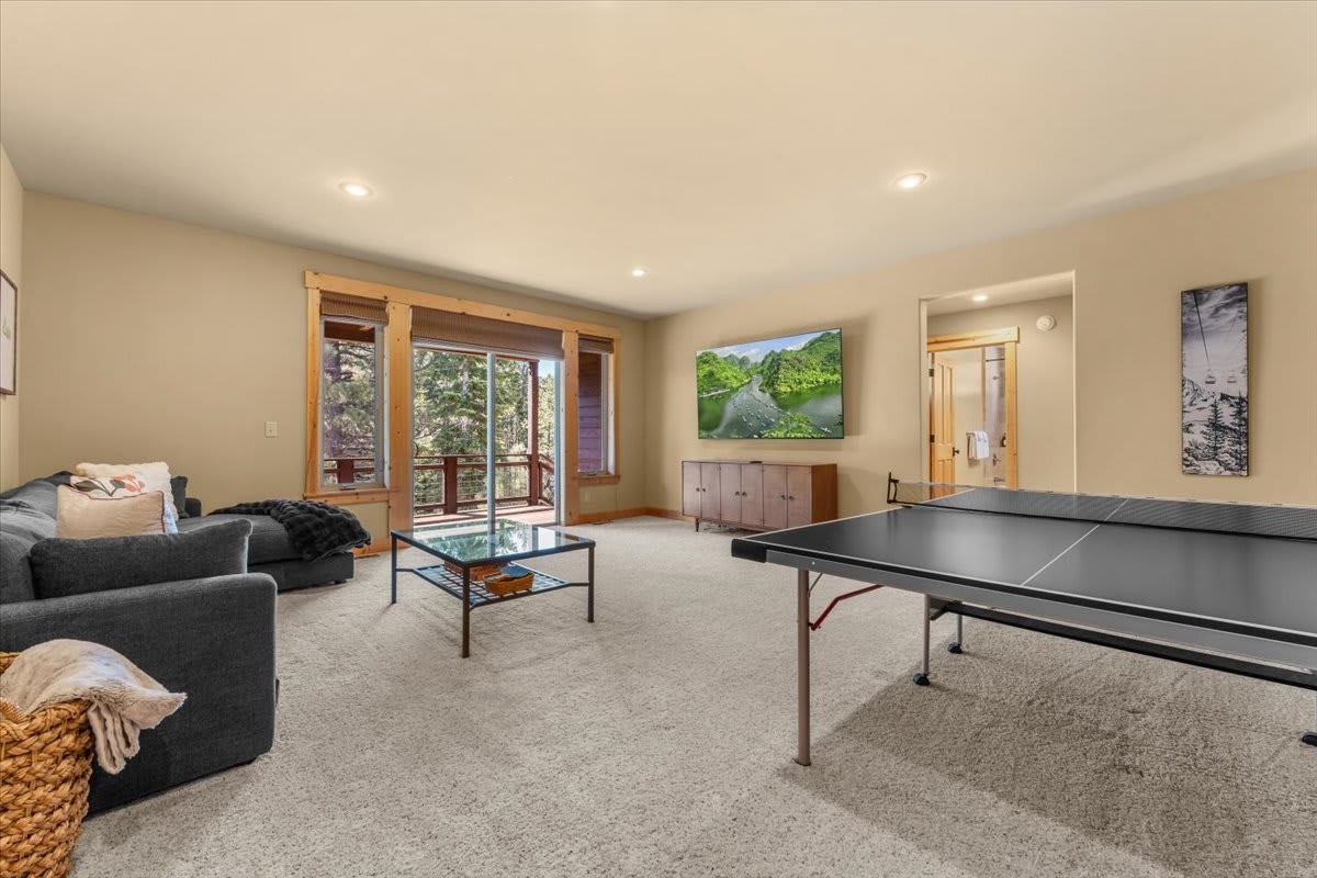 Spacious Truckee vacation rental with cozy living area, ping-pong table, and large windows overlooking a wooded view.