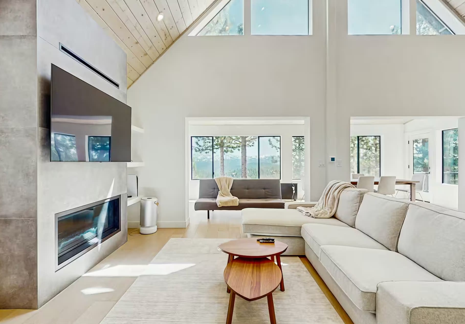 Modern living room with large windows in a Truckee vacation rental featuring a cozy sofa, TV, and fireplace.