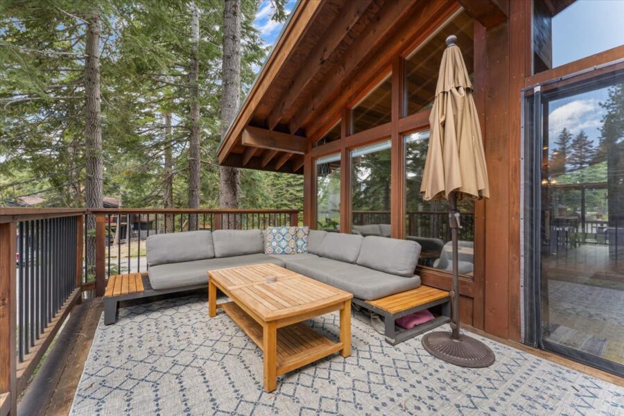 Cozy deck with sectional sofa and table at a vacation rental in Carnelian Bay, surrounded by tall trees.