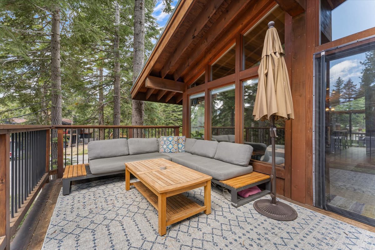 Cozy deck with sectional sofa and table at a vacation rental in Carnelian Bay, surrounded by tall trees.