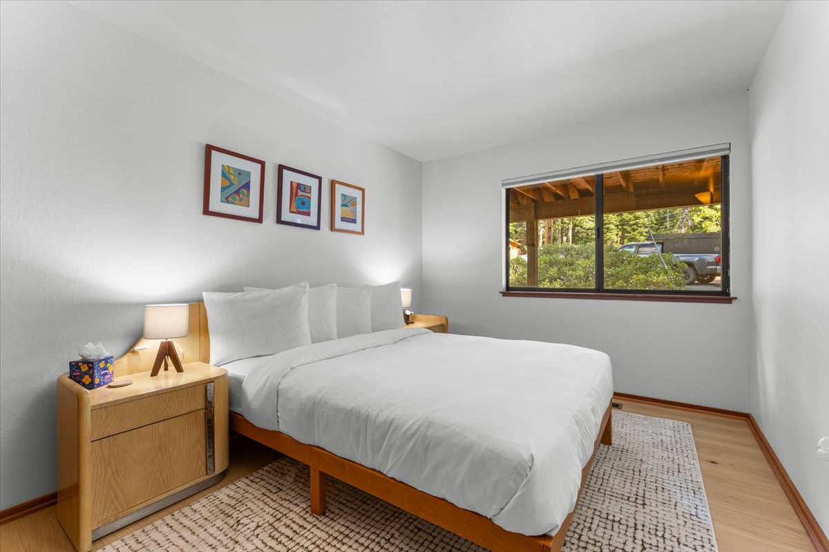 Cozy bedroom in a Carnelian Bay vacation rental with a large bed, stylish decor, and forest view through the window.