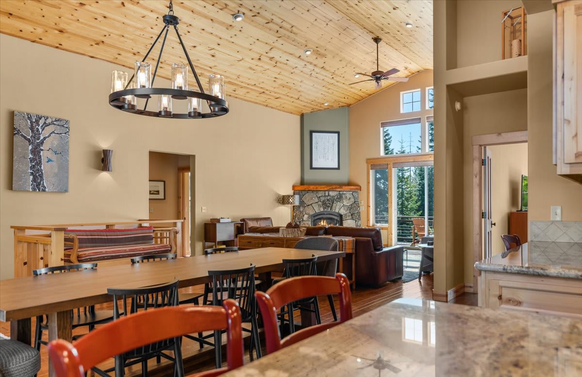 Spacious living area in a Truckee vacation rental with wood ceiling, modern chandelier, and stone fireplace.