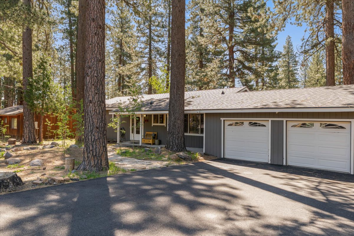 Gray vacation rental in Truckee, surrounded by tall pine trees, featuring a two-car garage and a cozy front porch.