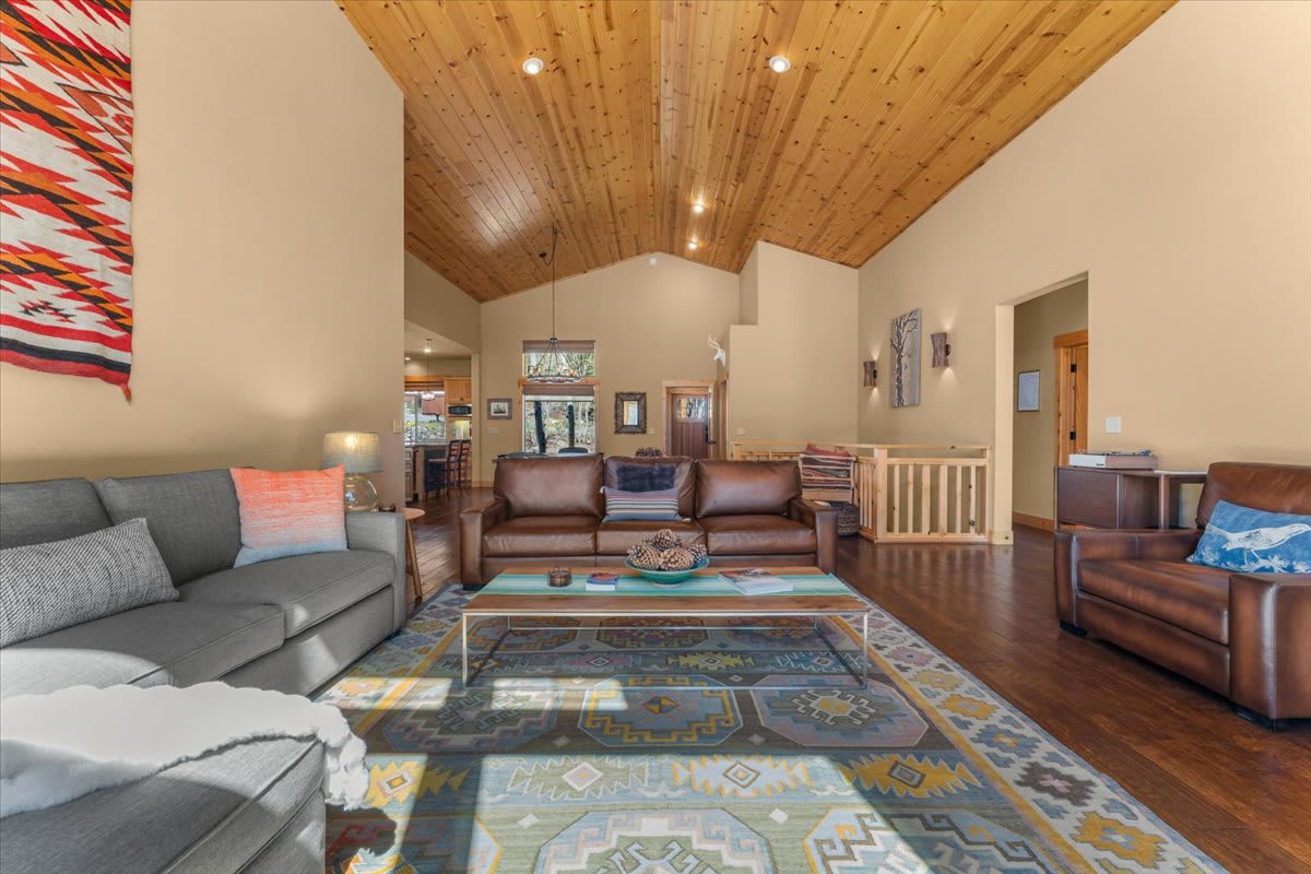 Spacious Truckee vacation rental living room with high wooden ceiling, cozy couches, and colorful patterned rug.