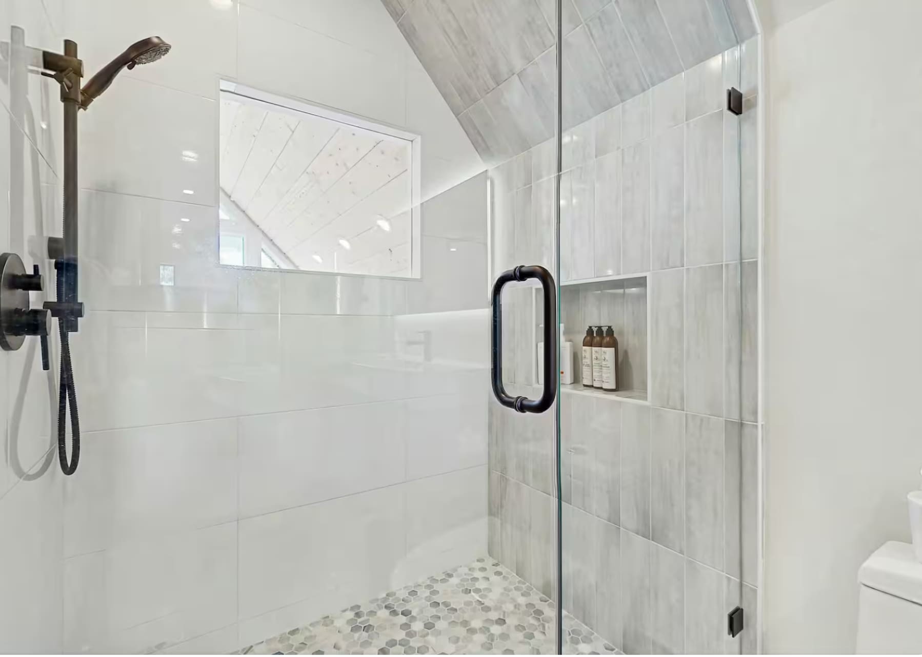 Modern shower in Truckee vacation rental, with glass door, rainfall showerhead, and recessed shelf in tiled wall.