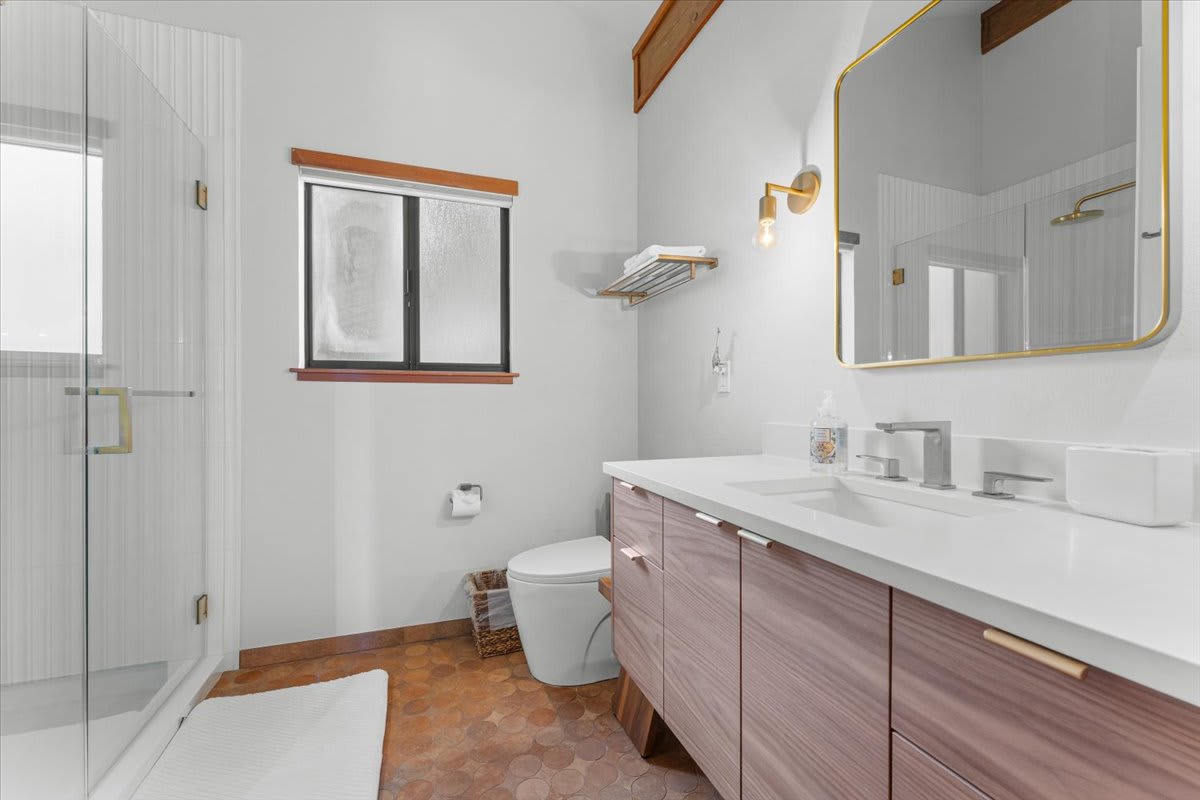 Modern bathroom in a Carnelian Bay vacation rental, featuring a large mirror, glass shower, and sleek wood cabinetry.