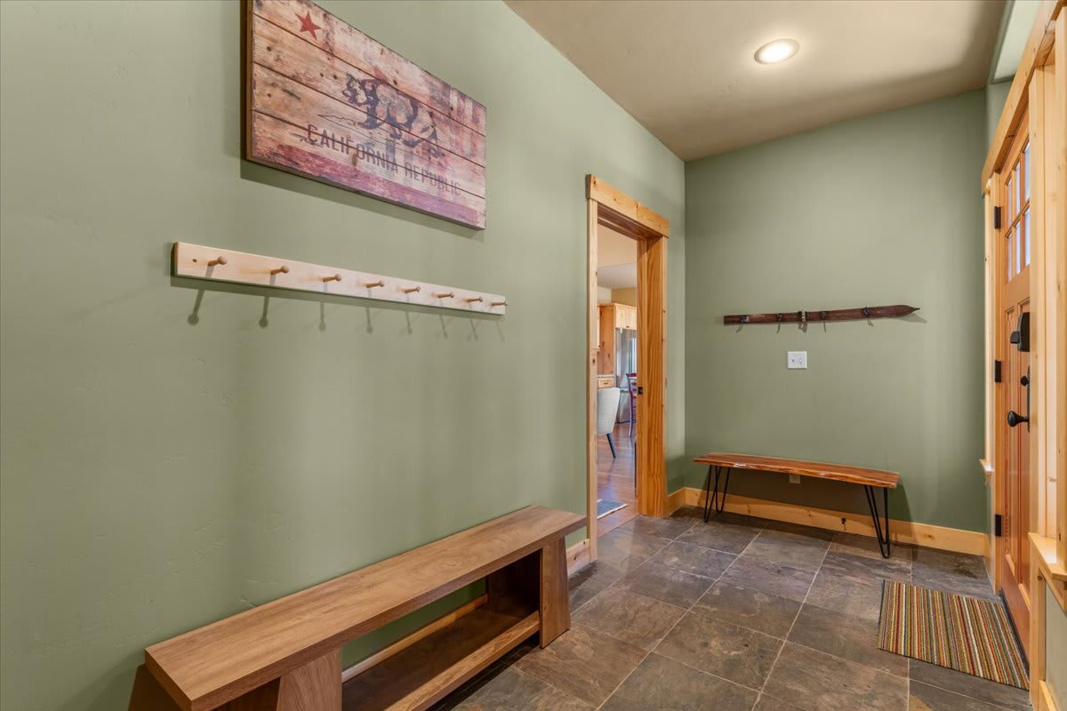 Entryway of a Truckee vacation rental with green walls, wooden benches, coat hooks, and a California Republic sign.