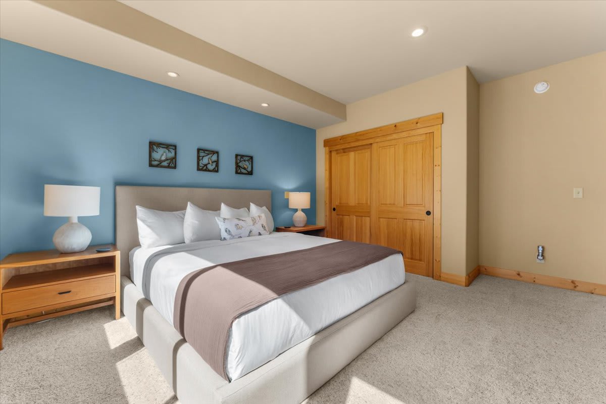 Bedroom in Truckee vacation rental with a large bed, blue accent wall, wooden doors, and soft lighting.