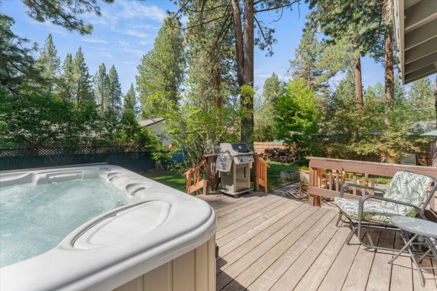 Truckee vacation rental with hot tub and deck featuring outdoor seating and grill, surrounded by tall pine trees.