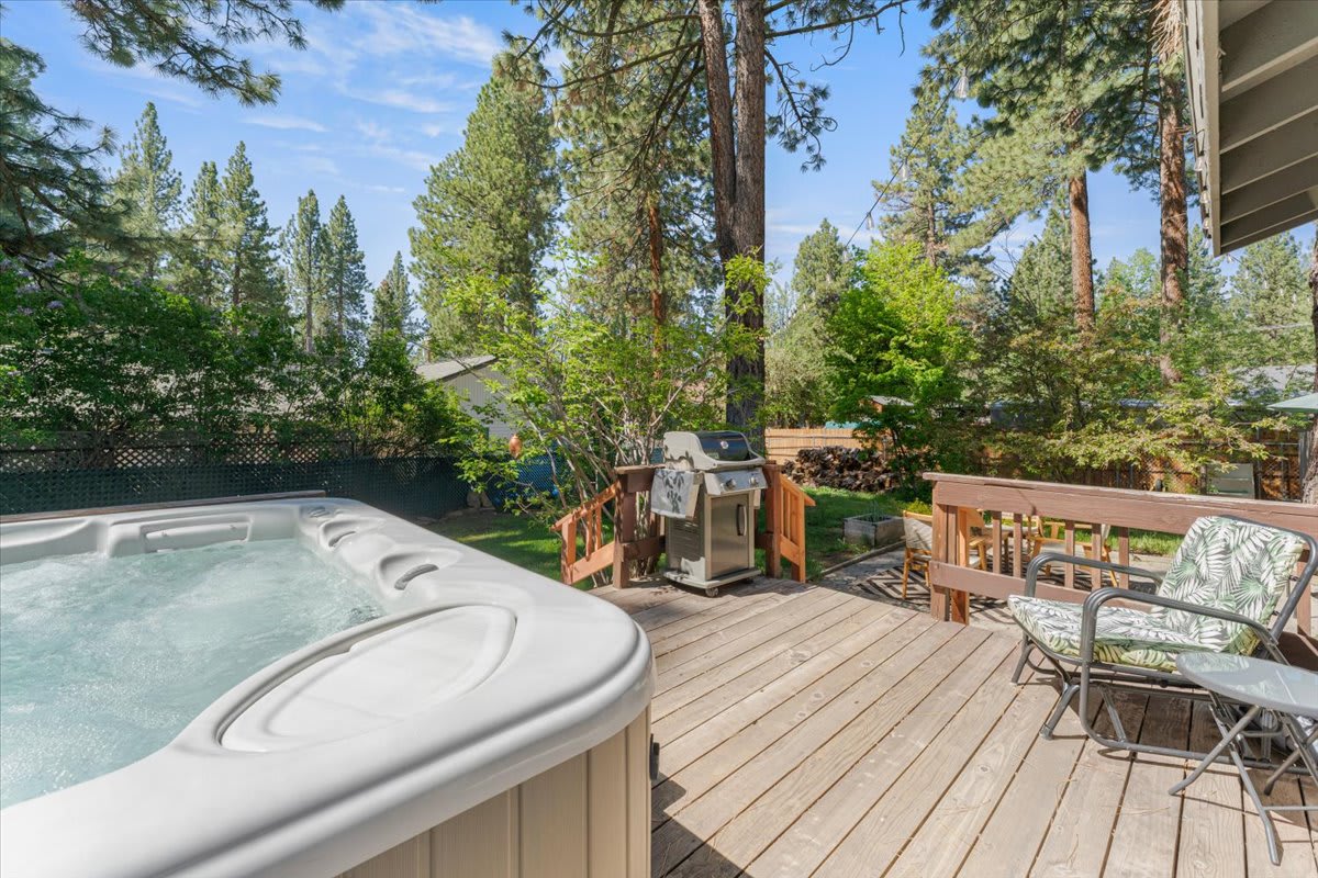 Truckee vacation rental with hot tub and deck featuring outdoor seating and grill, surrounded by tall pine trees.