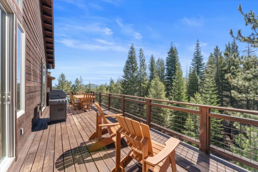 Wooden deck at a Truckee vacation rental, overlooking lush pine trees, with chairs and a barbecue grill.