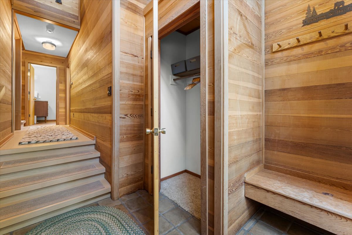 Wood-paneled hallway and stairs in Carnelian Bay vacation rental, featuring an open closet and bench.