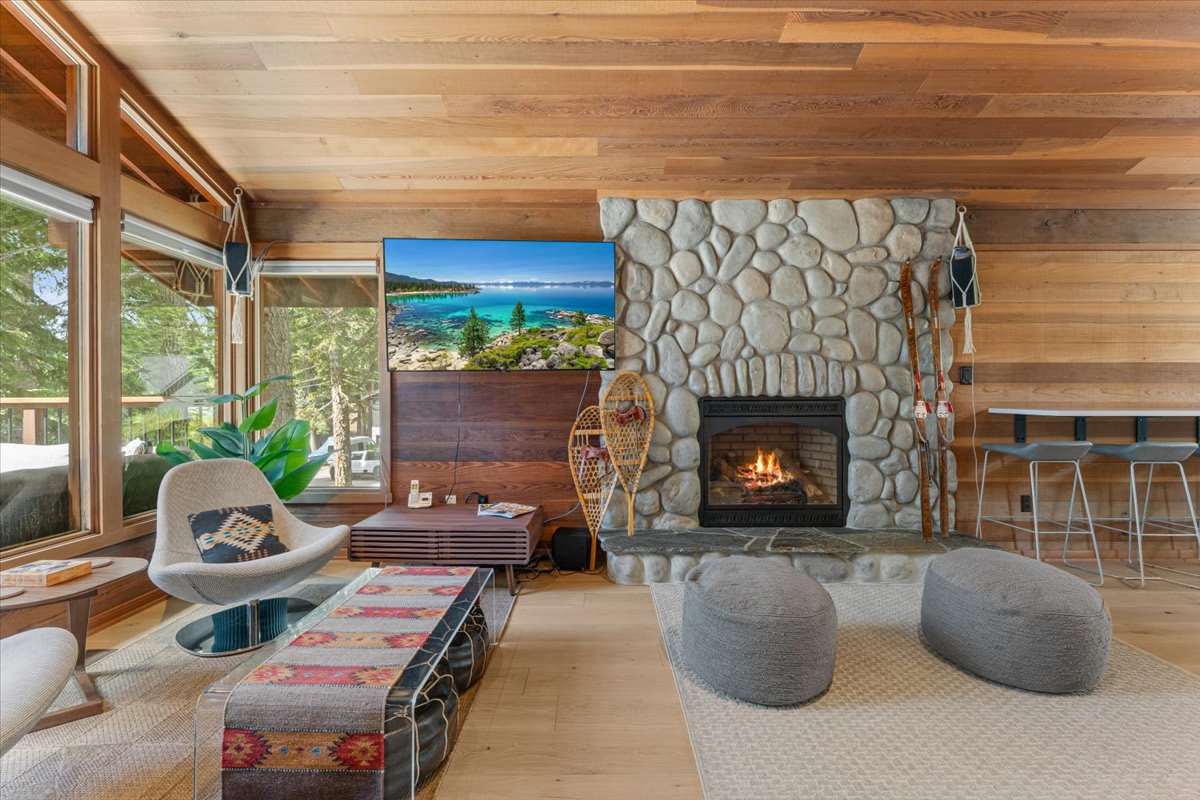 Cozy living room in a Carnelian Bay vacation rental with a stone fireplace, modern furniture, and forest views.