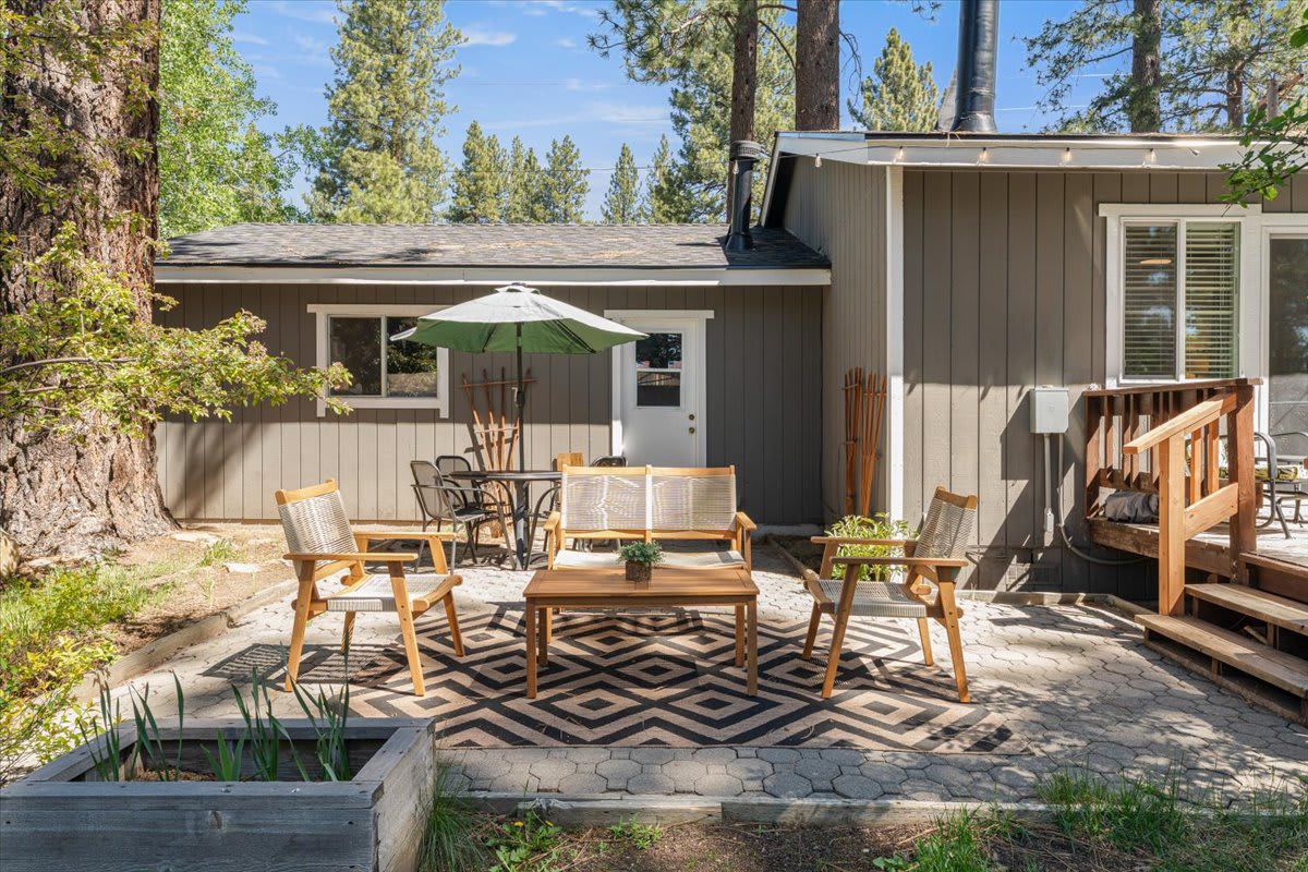Cozy patio with wooden chairs and umbrella at a Truckee vacation rental, surrounded by pine trees.