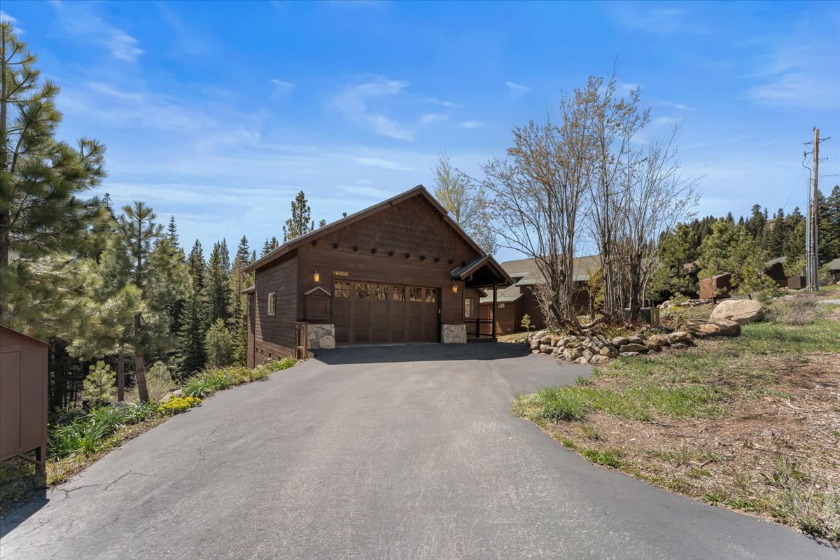 Wooden vacation rental cabin with trees in Truckee, featuring a sloped driveway and surrounded by nature under a blue sky.