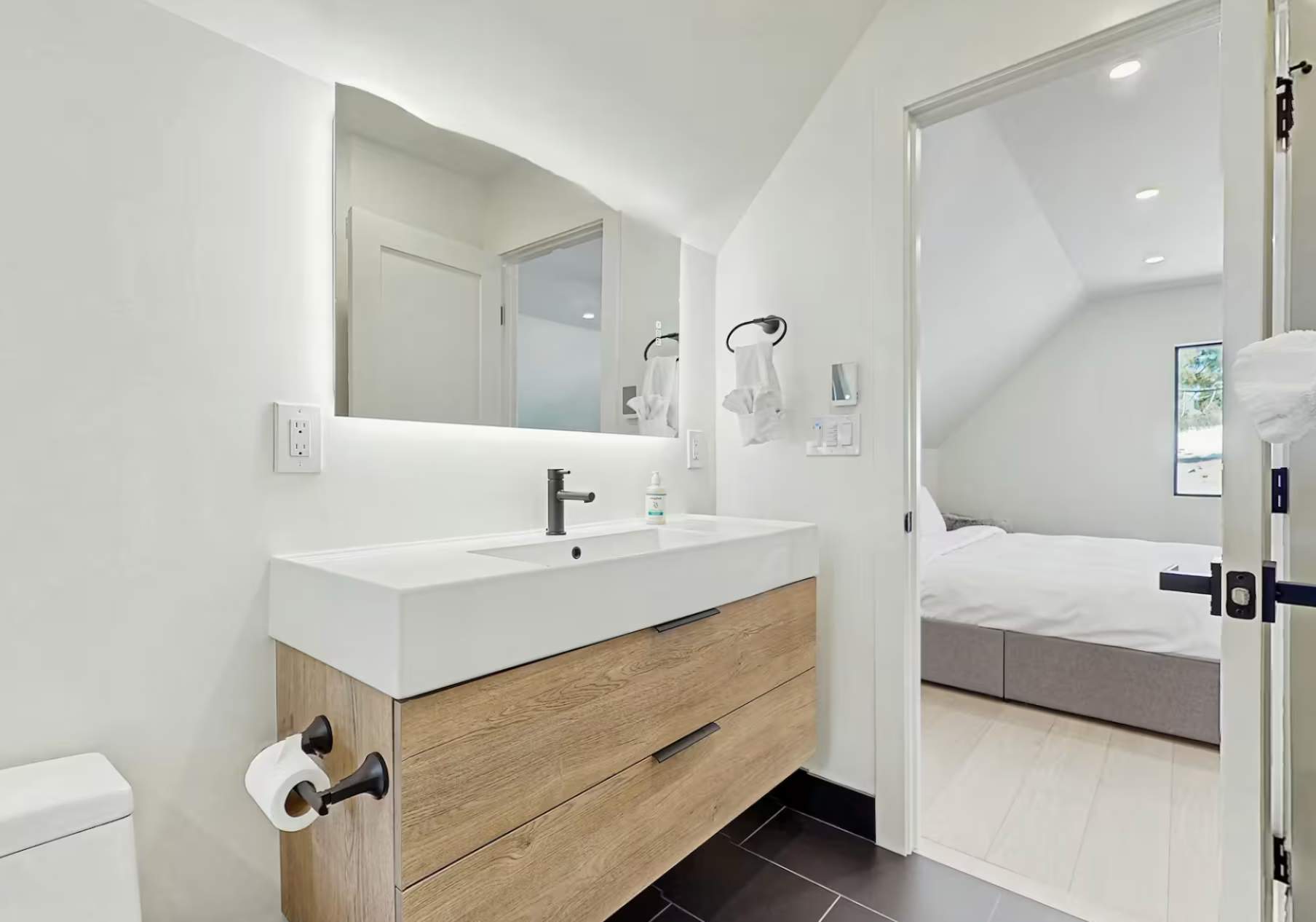 Modern bathroom in a Truckee vacation rental with a wood vanity, large mirror, and view into a cozy bedroom.