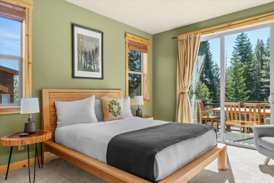 Cozy bedroom in a Truckee vacation rental with a view of pine trees through glass doors and a wooden balcony.