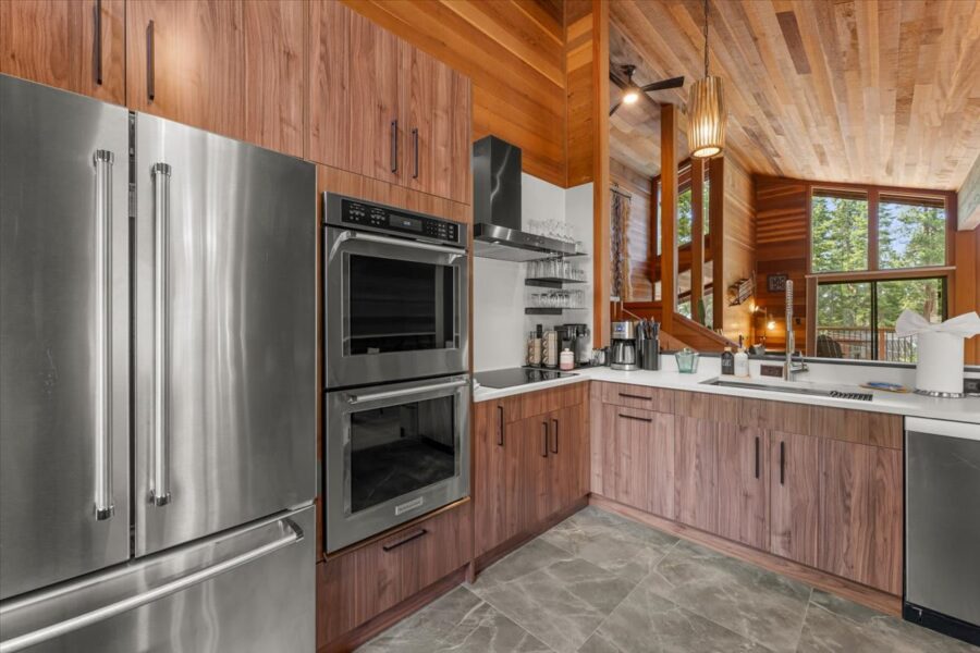 Modern kitchen in a Carnelian Bay vacation rental, featuring stainless appliances, wood cabinets, and large windows with forest views.
