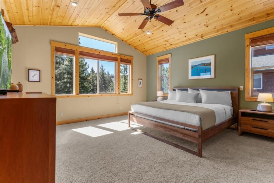 Spacious bedroom in a Truckee vacation rental with a large bed, wooden ceiling, and forest views through big windows.