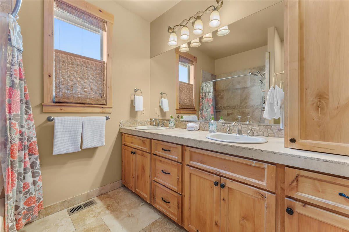 Rustic bathroom in Truckee vacation rental with wooden cabinetry, double sinks, floral curtain, and neutral tones.