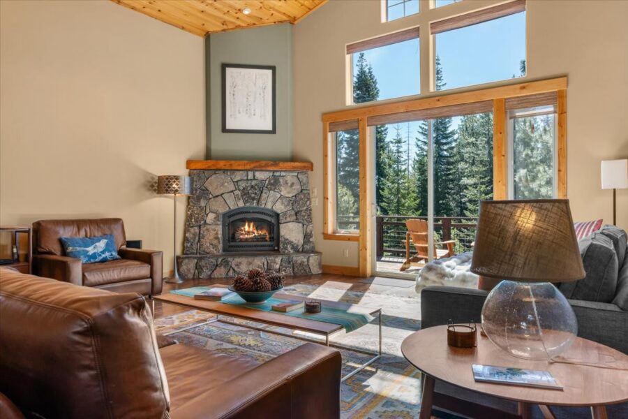 Cozy living room in a Truckee vacation rental with a stone fireplace and large windows overlooking pine trees.