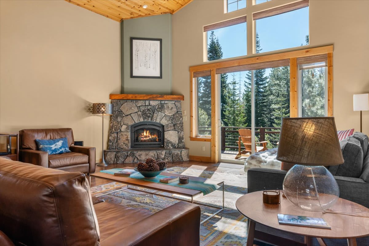 Cozy living room in a Truckee vacation rental with a stone fireplace and large windows overlooking pine trees.