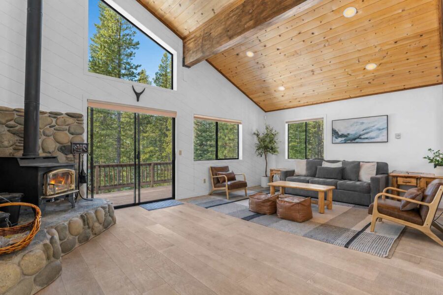 Spacious living room in a Truckee vacation rental with large windows, wooden ceiling, and cozy fireplace.