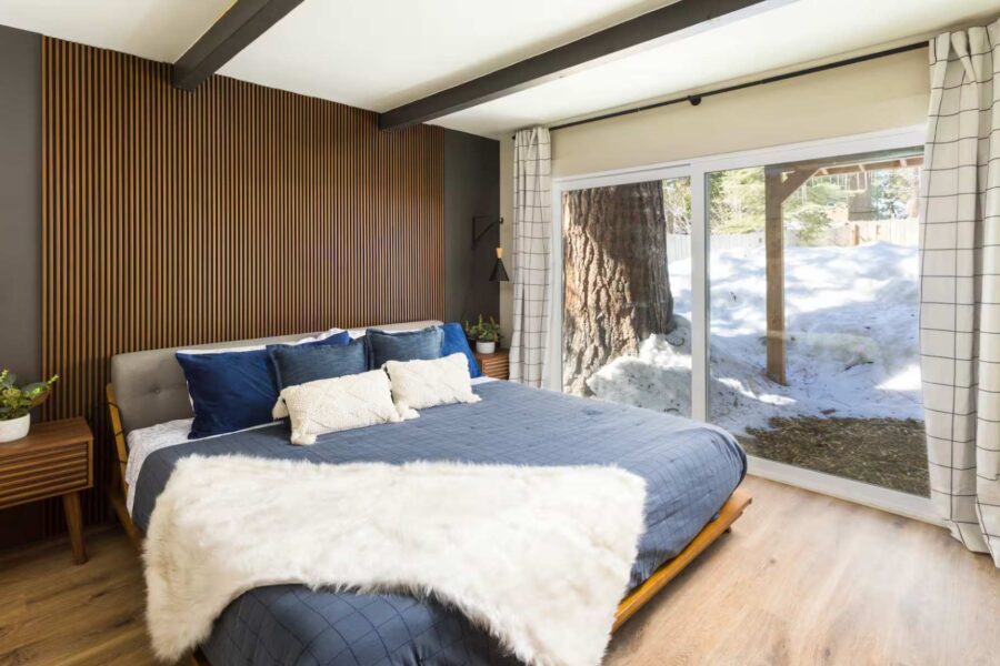 Stylish Kings Beach vacation rental bedroom with a cozy bed, wood accents, and snowy view through large window.