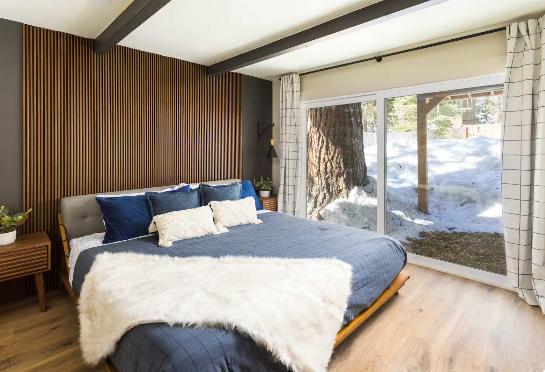 Stylish Kings Beach vacation rental bedroom with a cozy bed, wood accents, and snowy view through large window.