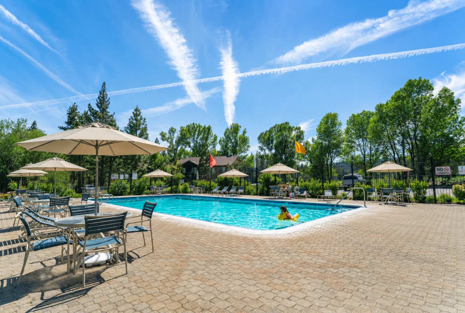 Sunny vacation rental in Tahoe City with a large pool, umbrellas, and lounge chairs surrounded by trees.