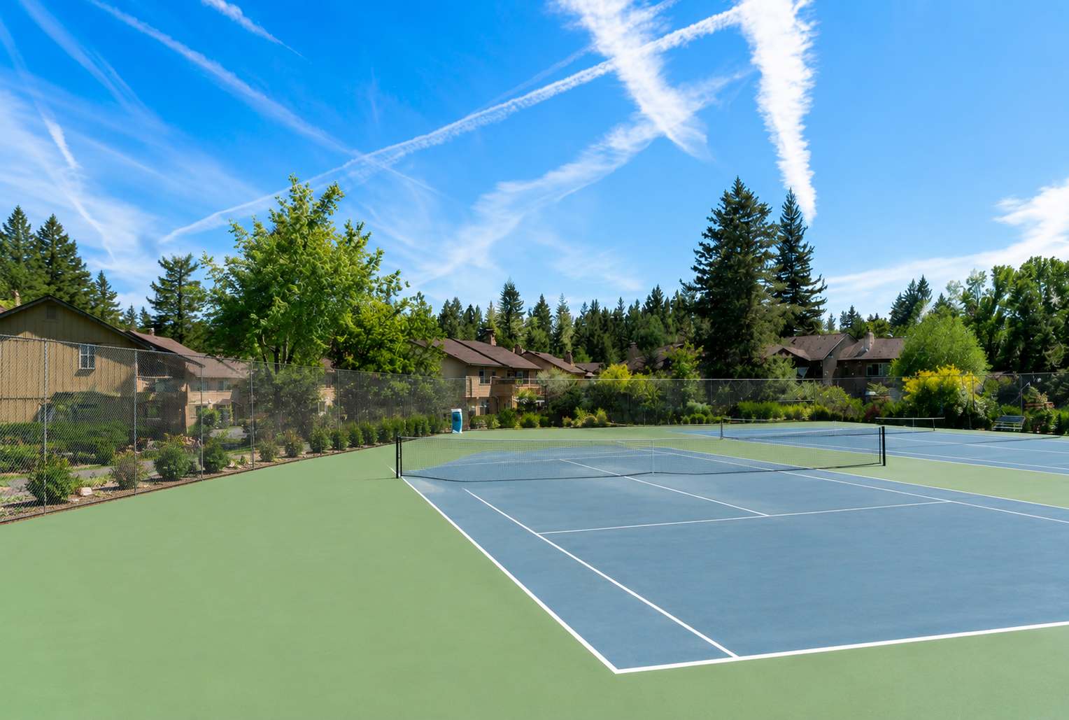 Tennis court next to vacation rentals, surrounded by trees in Tahoe City under a bright blue sky.