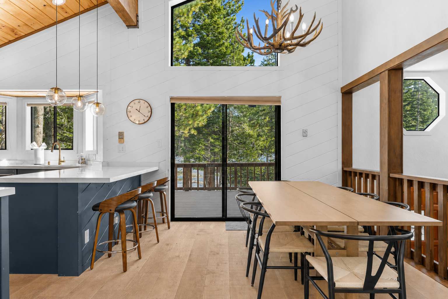 Modern kitchen and dining area in a Truckee vacation rental with forest views, antler chandelier, and sleek wooden furniture.