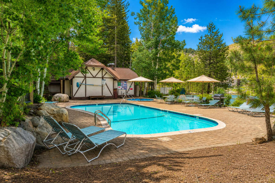 Outdoor pool at a vacation rental in Olympic Valley, surrounded by trees and lounge chairs under umbrellas.