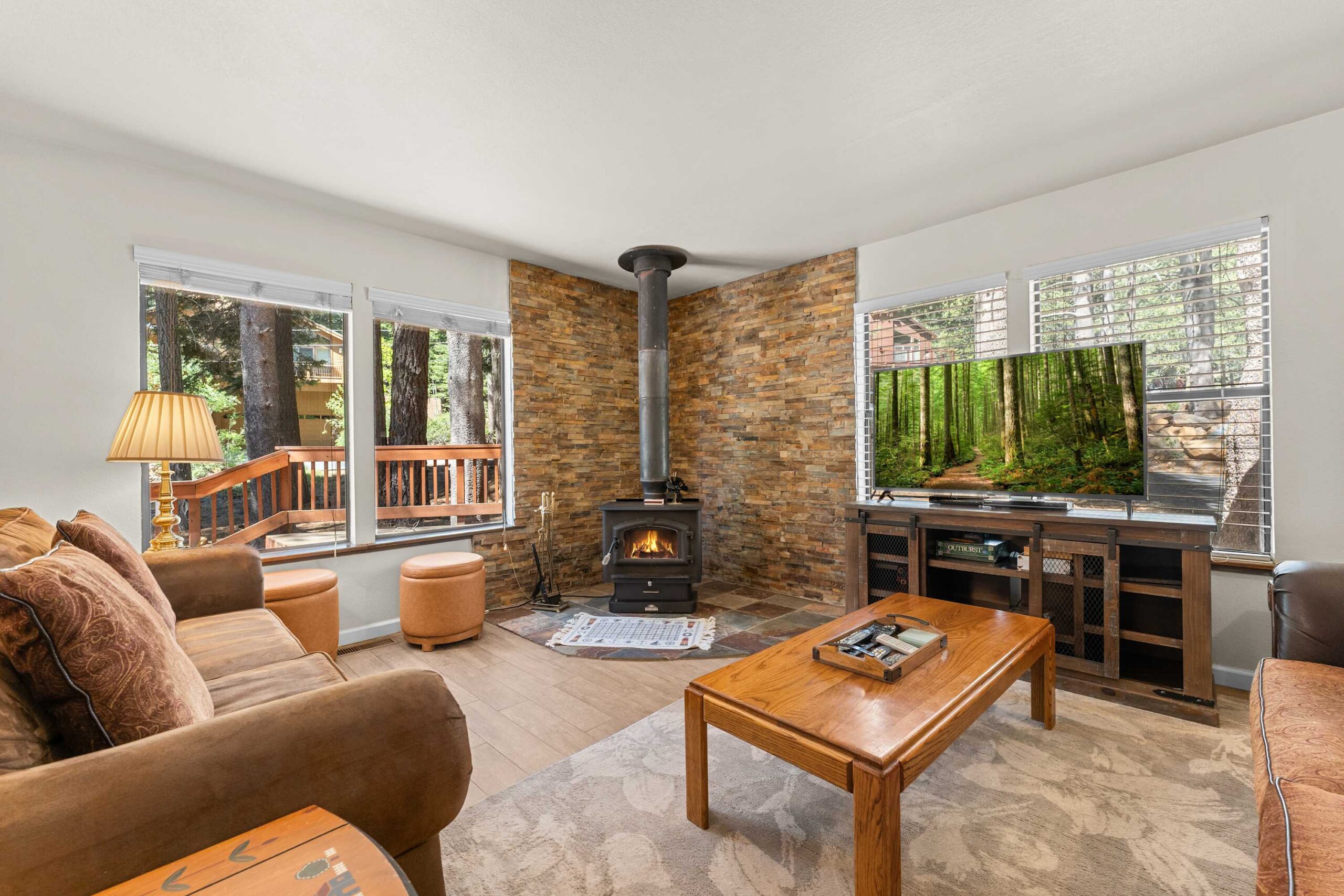 Cozy living room in Truckee vacation rental with a fireplace, TV, and forest view through large windows.