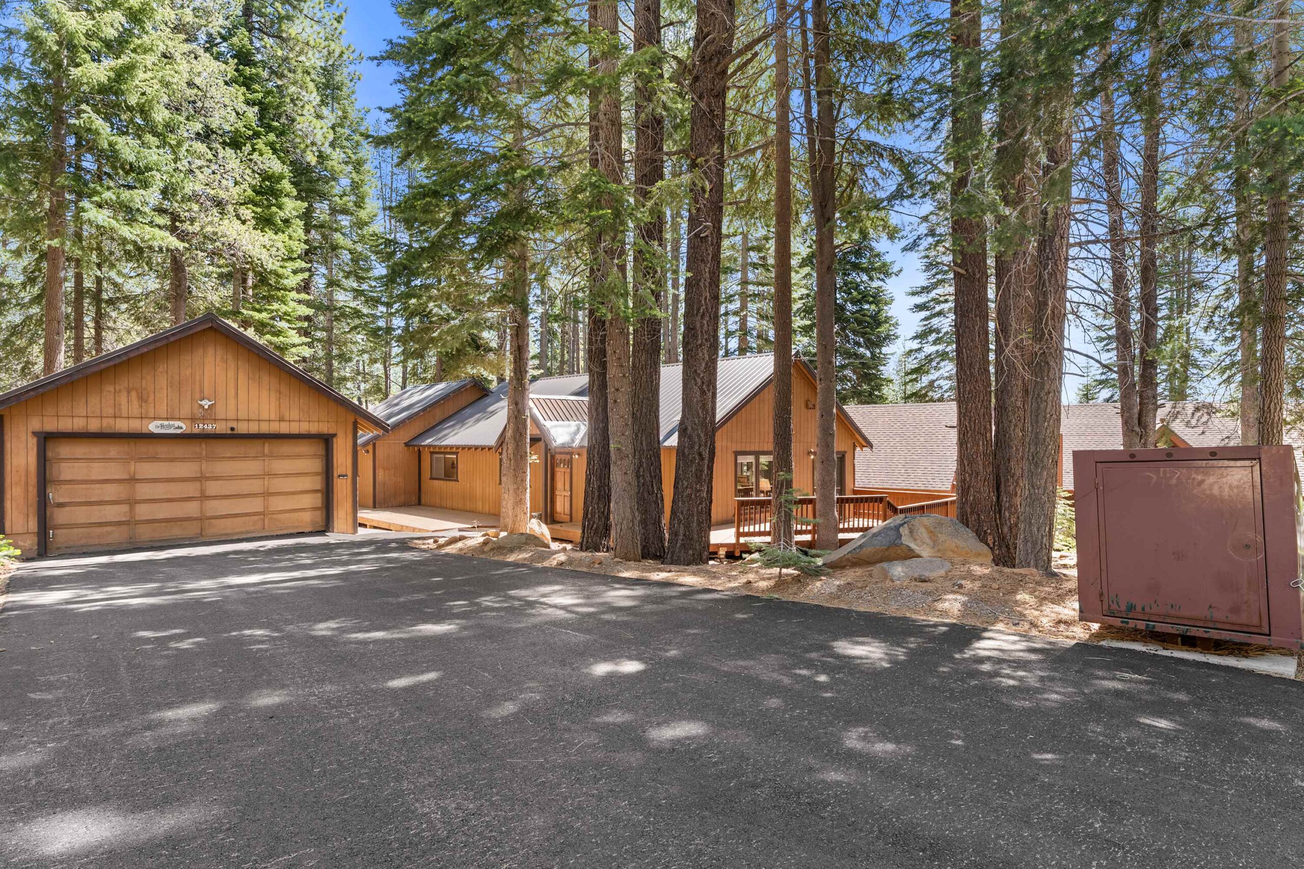 Wooden vacation rental cabin in Truckee, surrounded by tall pine trees with a spacious driveway and garage.