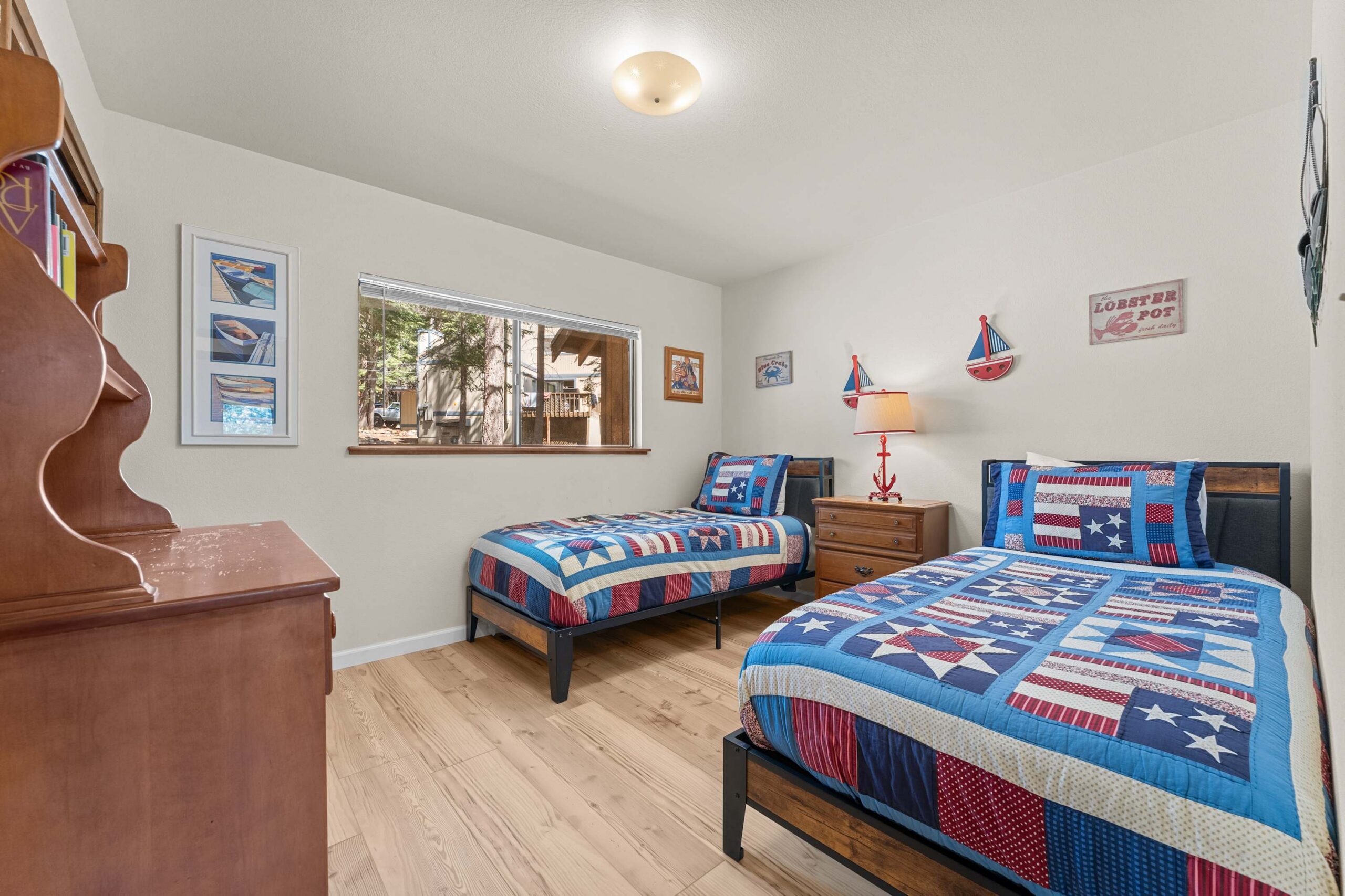 Cozy twin beds with colorful quilts in a Truckee vacation rental room, featuring nautical decor and a large window view.