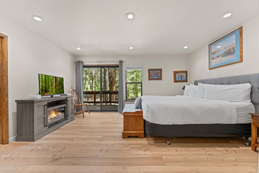 Modern bedroom in Truckee vacation rental with fireplace, TV, and balcony view of trees.