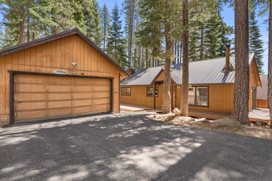 Wood cabin-style vacation rental in Truckee, surrounded by tall pine trees with a spacious driveway and garage.