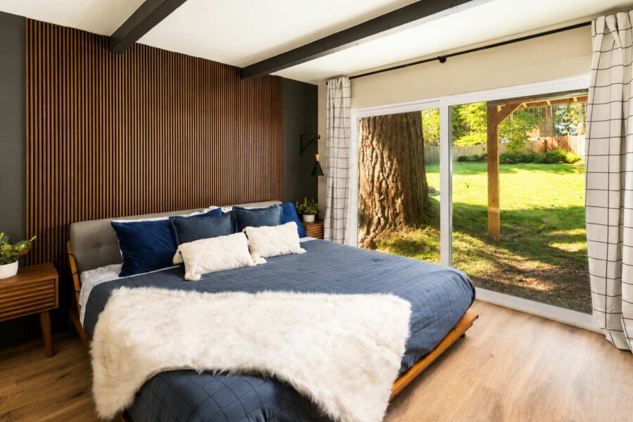 Bedroom in Kings Beach vacation rental with large window view of a tree and grassy yard. Cozy bed with blue linens.